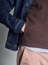 Wearing the Blue de Gênes Koi Wool Gilet in Chocolate over a brown fleece and light blue shirt, paired with beige pants, the person's torso and part of one arm are visible as they stand with one hand in their pocket.