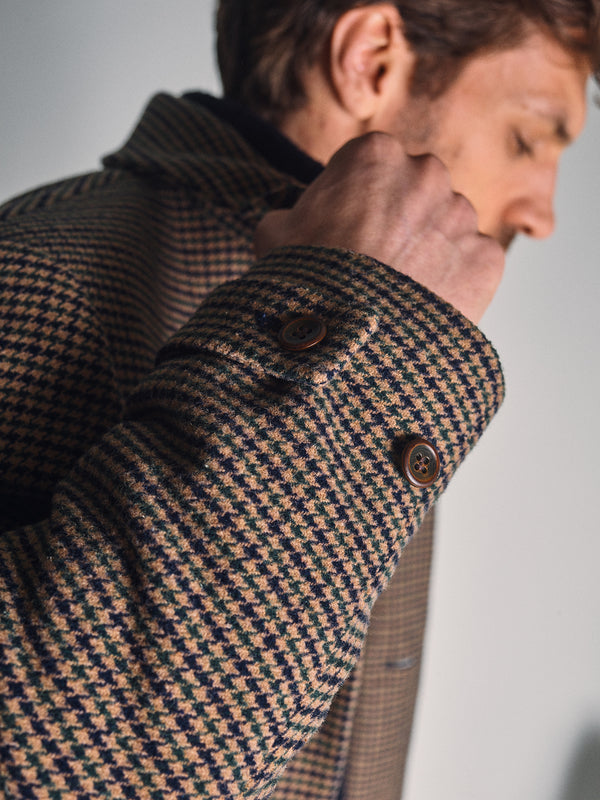 A close-up of a man wearing the Blue de Gênes Massone Check Coat in multi check, highlighting the sleeve and buttons, with his face softly out of focus in the background.