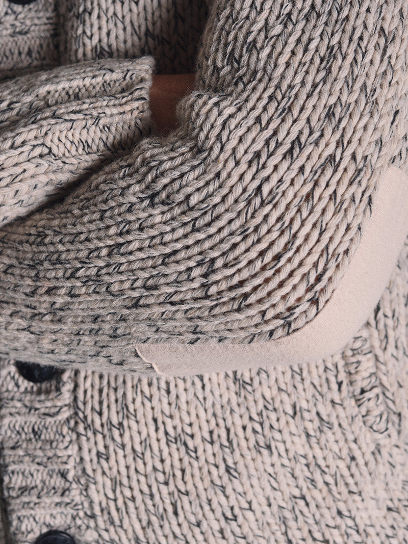 Close-up of a person’s arm crossed over their chest, wearing the Sakura Knit Cardigan in Stone by Blue de Gênes, featuring chunky knit texture and visible stitching.
