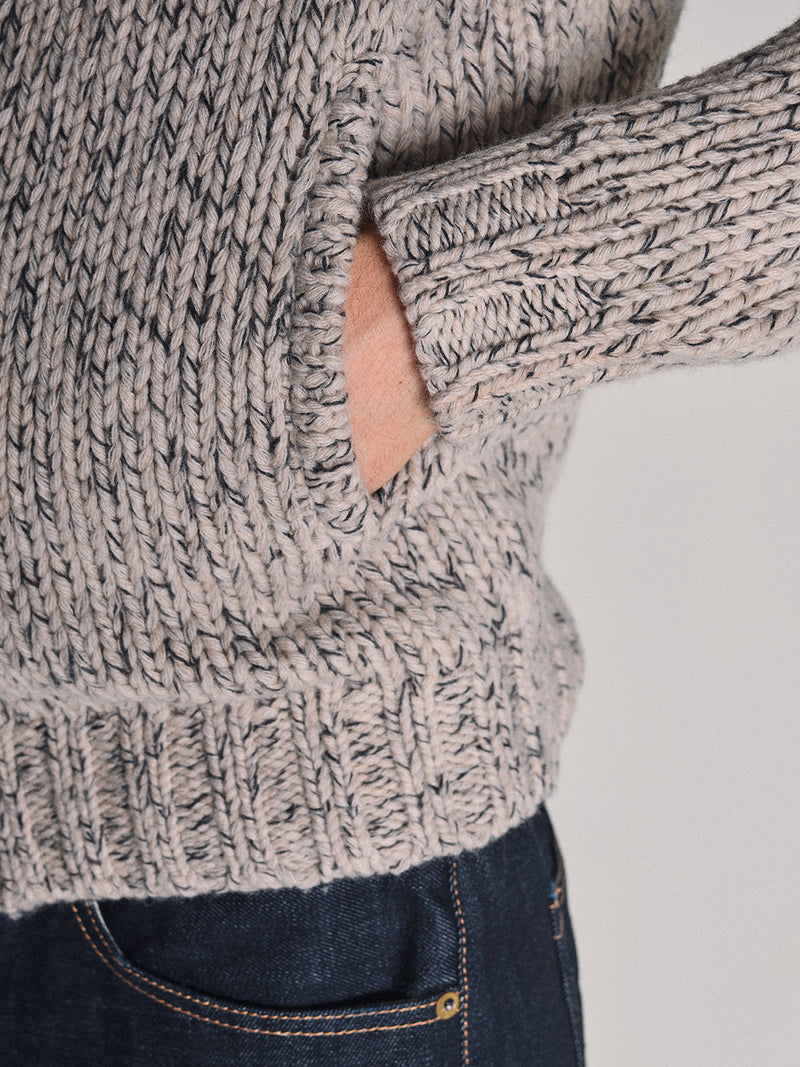 A person wearing the Blue de Gênes Sakura Knit Cardigan in Stone, with their hand in a side pocket, paired with dark blue jeans.