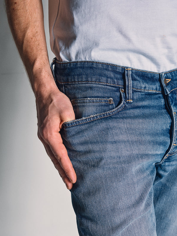 A person in Blue de Gênes Vinci Girisha Used Jeans and a white tee stands with their left hand in the jean pocket, shown from waist to mid-thigh.