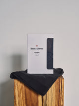 A box labeled Blue de Gênes BdG Boxershorts - 3 Pack - Black stands on a folded black garment atop a wooden block against a light gray background, showcasing breathable boxer shorts designed for all-day comfort.
