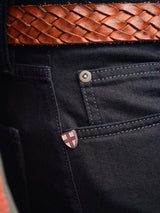 Close-up of Vinci Venom Blk Jeans - Dark Denim by Blue de Gênes, regular fit and made in Italy, showing a shield emblem on the pocket and styled with a brown woven leather belt.