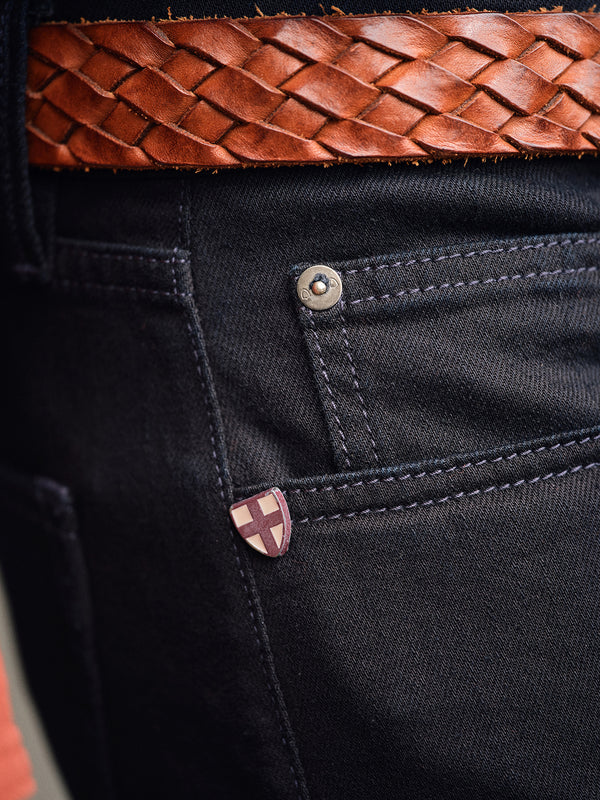 Close-up of Vinci Venom Blk Jeans - Dark Denim by Blue de Gênes, regular fit and made in Italy, showing a shield emblem on the pocket and styled with a brown woven leather belt.