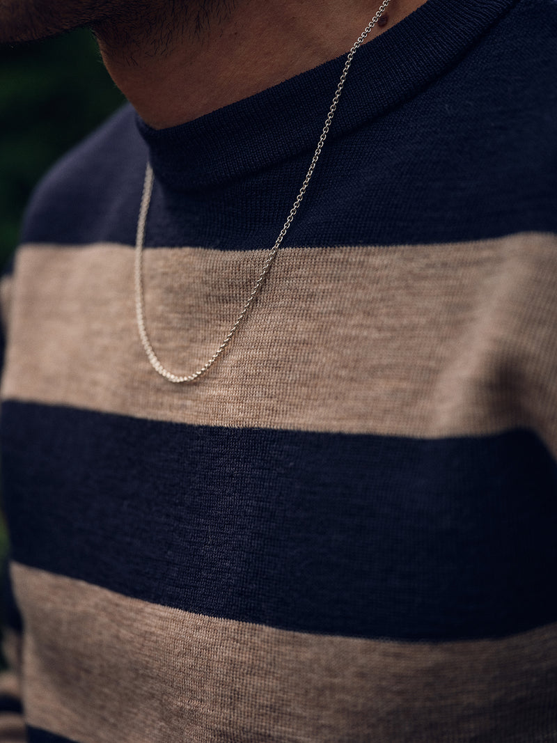 A person wearing the Blue de Gênes Toyama Stripe Knit L/S in Dark Navy and a thin silver chain necklace, with only the lower face, neck, and upper torso visible.