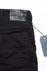 Close-up of the back pocket and waistband of Blue de Gênes Repi 3325 Black Jeans in durable black denim, featuring a black leather brand patch and a blue tag attached by string.