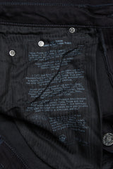 Close-up of the inside of Blue de Gênes Repi 3325 Black Jeans, showing white printed text on durable black denim with visible rivets and a button. The text describes the jeans and their inspiration.