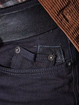 Close-up of the front pocket and waistband of Blue de Gênes Repi 3325 Black Jeans in durable black denim, featuring a black belt and a brown corduroy jacket at the top right corner.